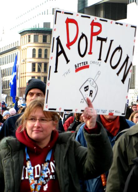 Woman holds sign that says 'Adoption: The <strong>Better</strong> Choice!'
