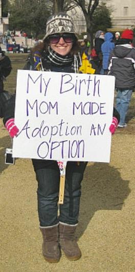 Young woman holds sign that says, 'My Birth Mom Made Adoption an Option'