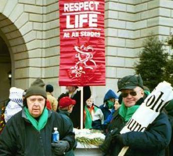 Two older men in front of red banner that says, 'Respect Life At All Stages'
