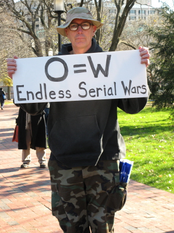 Man in fatigues carries sign: 'O=W/Endless Serial Wars'