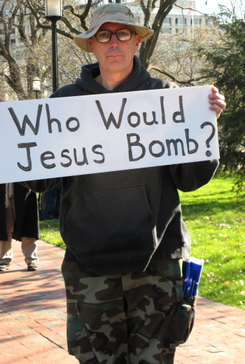 Man in fatigues shows the other side of his sign: 'Who Would Jesus Bomb?'