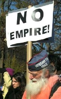 White-bearded man, whose cap says 'Veterans for Peace,' holds sign that says 'No Empire!'