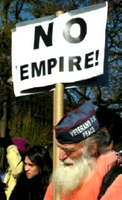 White-bearded man wears 'Veterans for Peace' cap and carries sign that says, 'NO EMPIRE!'