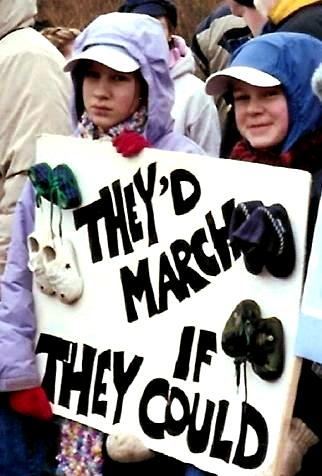 Two children with sign that holds baby shoes and says 'They'd March If They Could'
