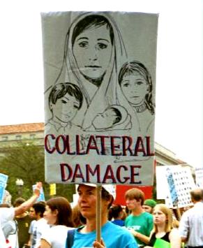 Woman holds sign that says 'Collateral Damage' and includes picture of woman (in headscarf) with her three children